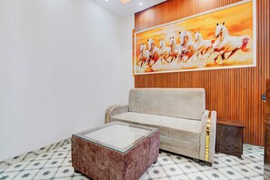 A room with a sofa, a glass coffee table, and a wooden panel wall with a painting of horses.