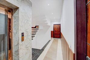 A hallway with a marble wall, a wooden door, and a staircase leading to another floor.