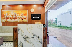 Un área de recepción con un panel de pared de madera, un reloj, un letrero que indica 'TOWNHOUSE' y 'oyo-serviced', y un cuadro grande de caballos.