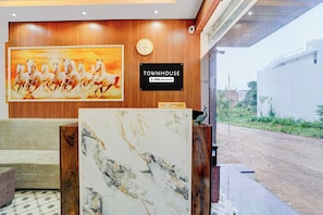 A reception area with a wooden panel wall, a clock, a sign indicating 'TOWNHOUSE' and 'oyo-serviced', and a large painting of horses.