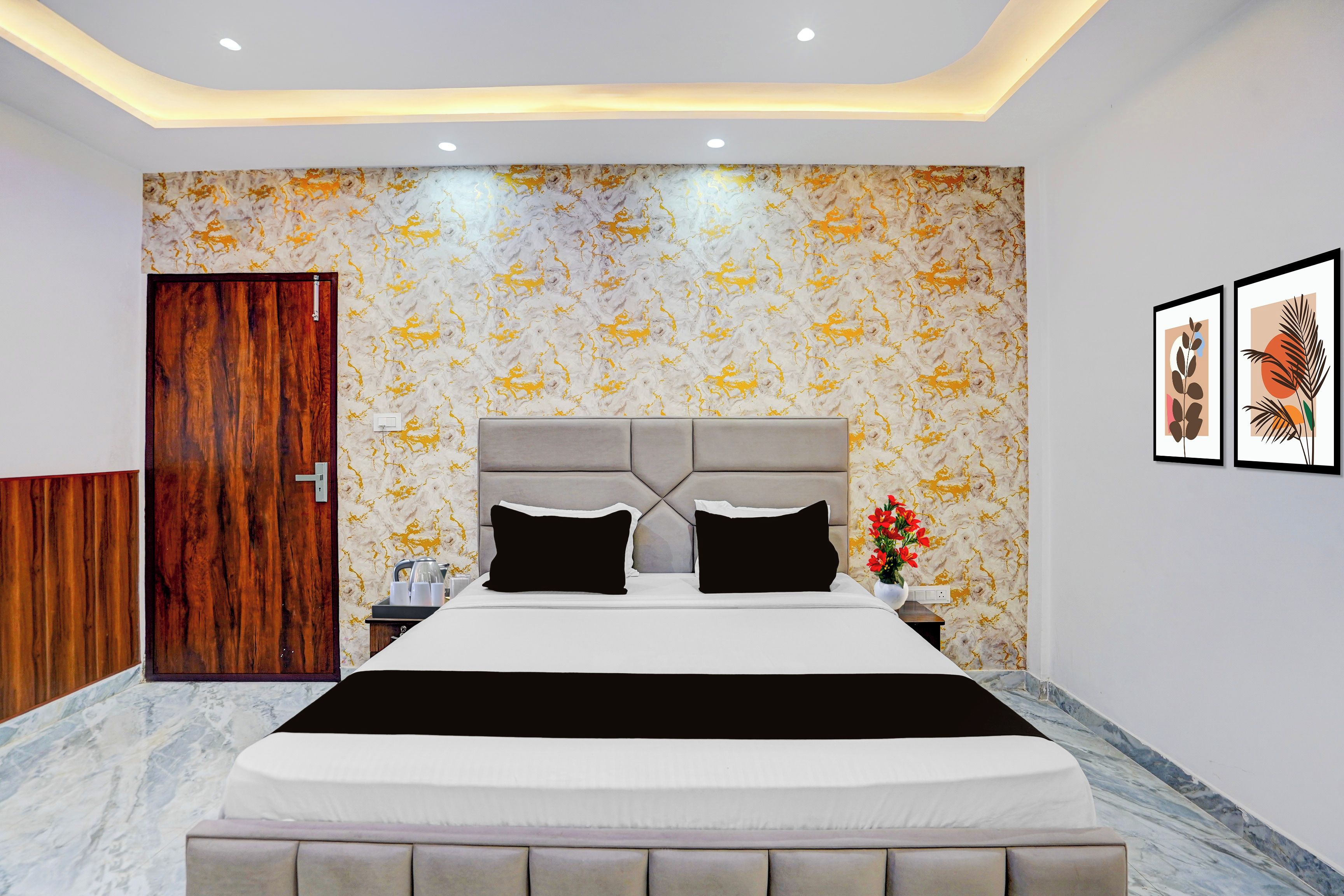 A modern bedroom with a marble-patterned wall, a tufted headboard, and a nightstand with a vase of flowers.