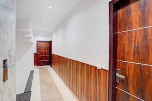 Un passadís amb una porta de fusta, un mur de marbre i una escala que condueix a una altra habitació.