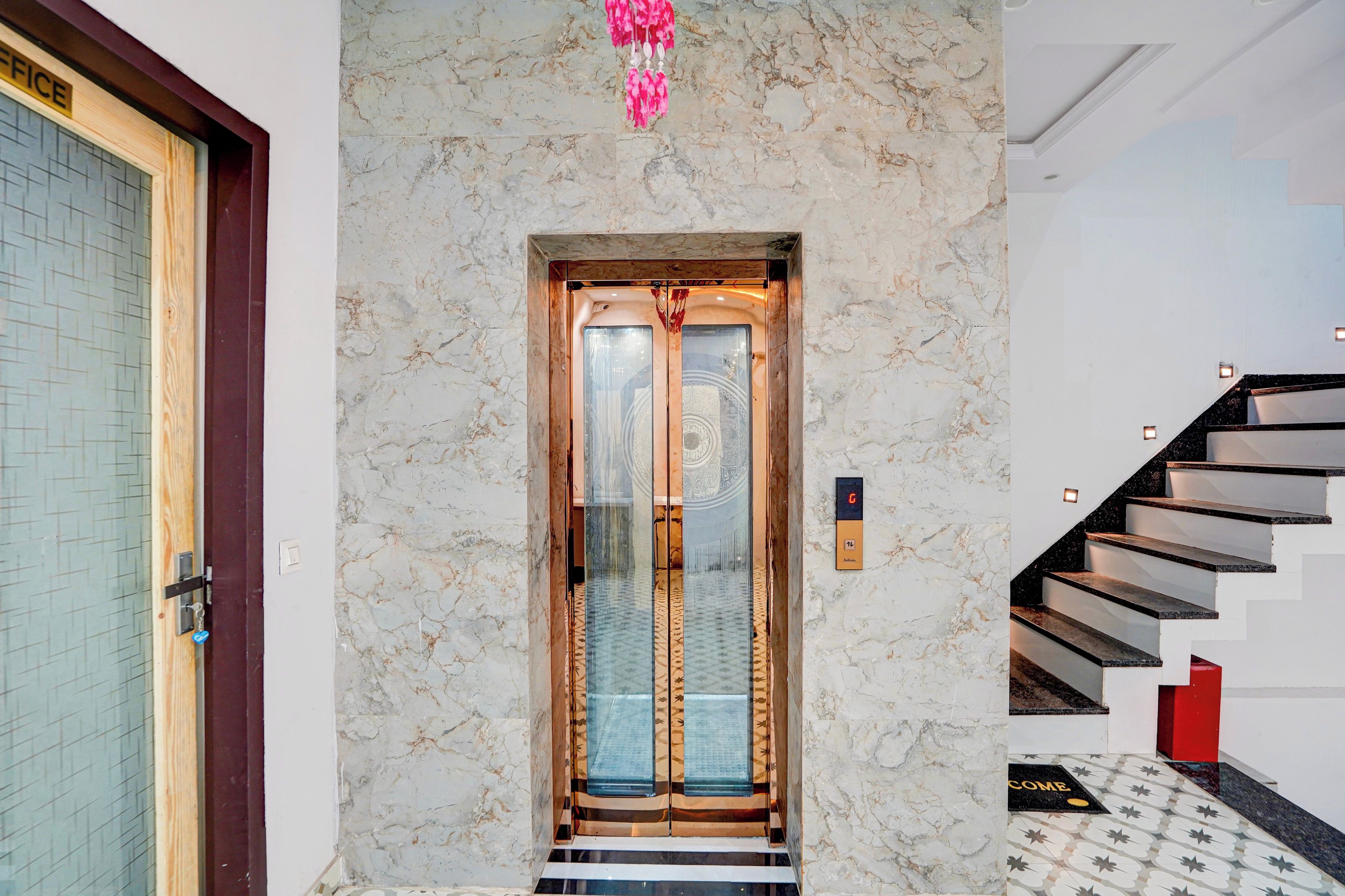 A marble wall with a modern elevator and a staircase with a red accent.