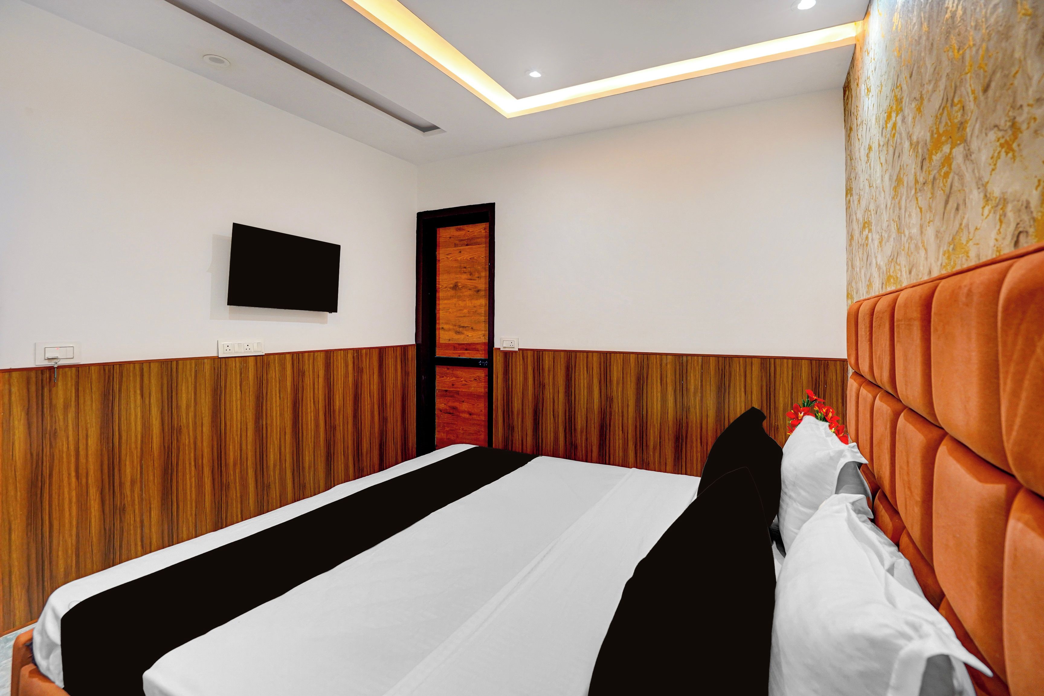 A hotel room with a bed, a flat-screen TV mounted on the wall, and a wooden door.