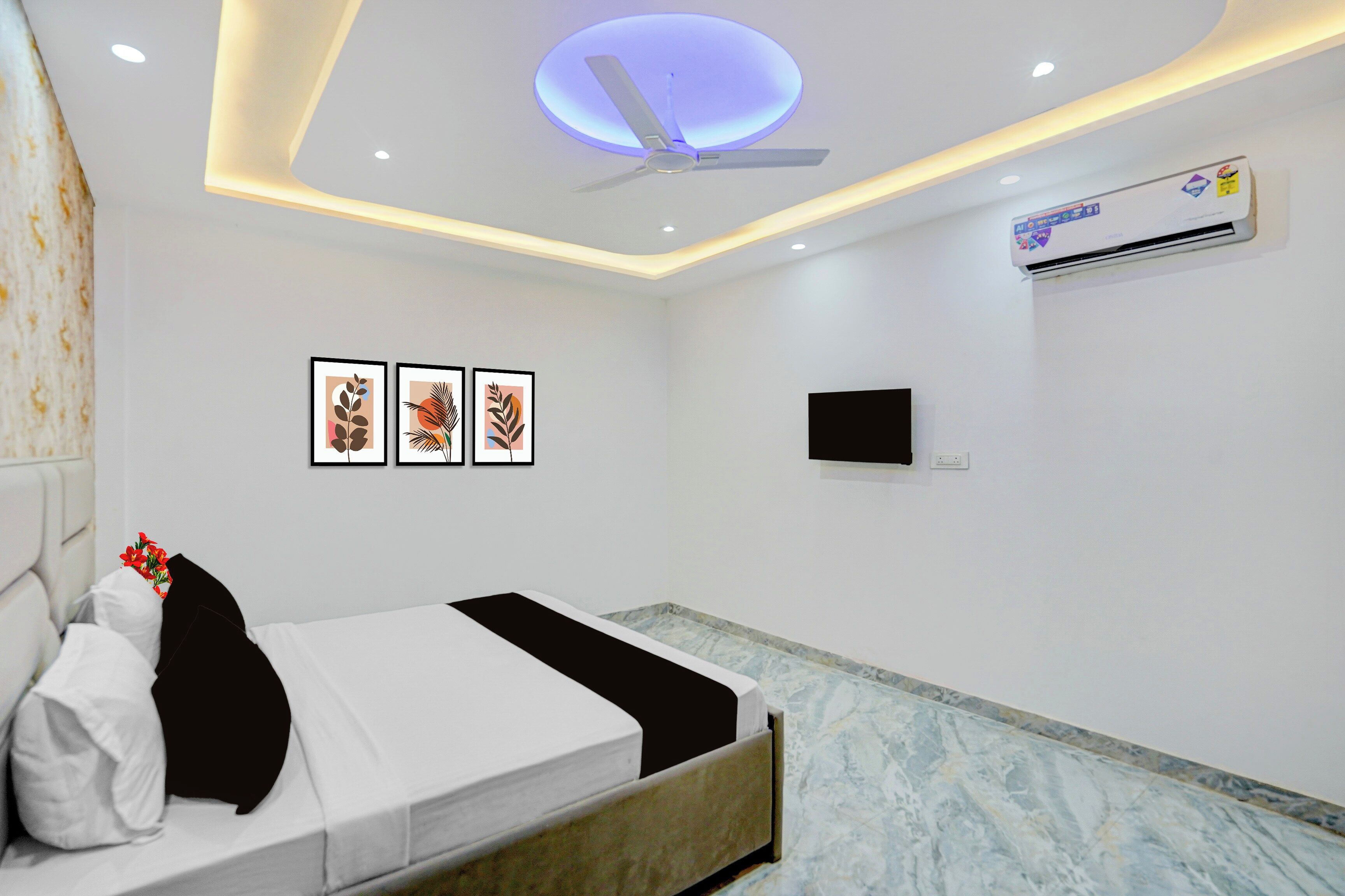 A hotel room with a bed, a ceiling fan, wall-mounted air conditioning, and framed artwork.