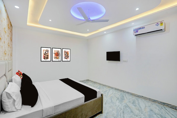 A hotel room with a bed, a ceiling fan, wall-mounted air conditioning, and framed artwork.