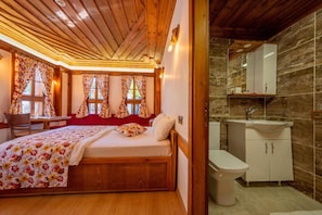 Un dormitorio con techo de madera, una cama con ropa de cama floral, un escritorio y un baño con lavabo y espejo.