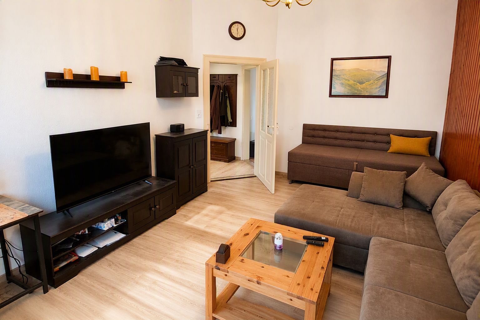 Ein Wohnzimmer mit Flachbildfernseher, dunklem Holzmöbel, einem braunen Sofa, einem Glastisch und einem Gemälde an der Wand.