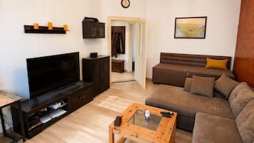 Ein Wohnzimmer mit Flachbildfernseher, dunklem Holzmöbel, einem braunen Sofa, einem Glastisch und einem Gemälde an der Wand.