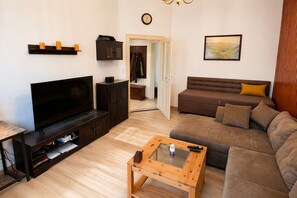 A living room with a flat-screen TV, dark wooden furniture, a brown sofa, a glass coffee table, and a painting on the wall. - Garden Retreat – Spacious Apartment by Bodetal (Thale)