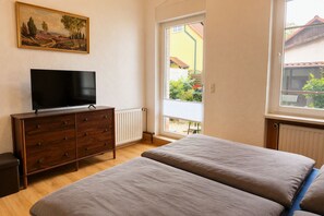 A bedroom with a TV on a dresser, a bed, a window with a view of the outside, and a radiator. - Garden Retreat – Spacious Apartment by Bodetal (Thale)