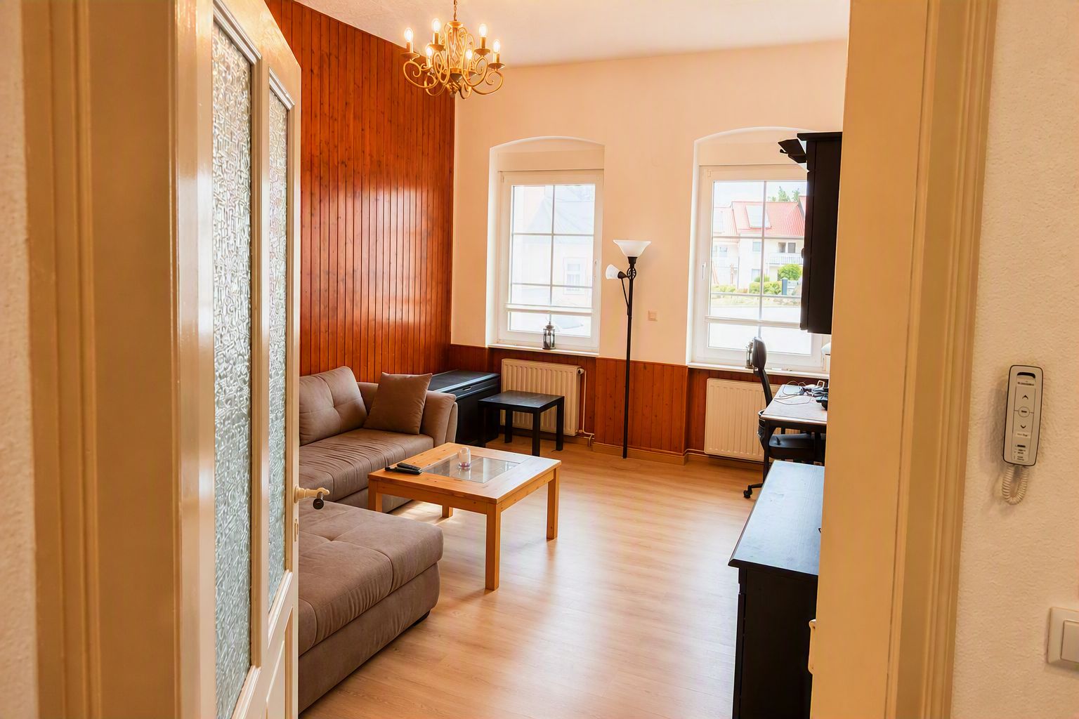 Ein Wohnzimmer mit einer Couch, einem Couchtisch und einem Essbereich mit Tisch und Stühlen. Eine Kristallleuchter, eine Lampe und ein Telefon sind an der Wand angebracht.