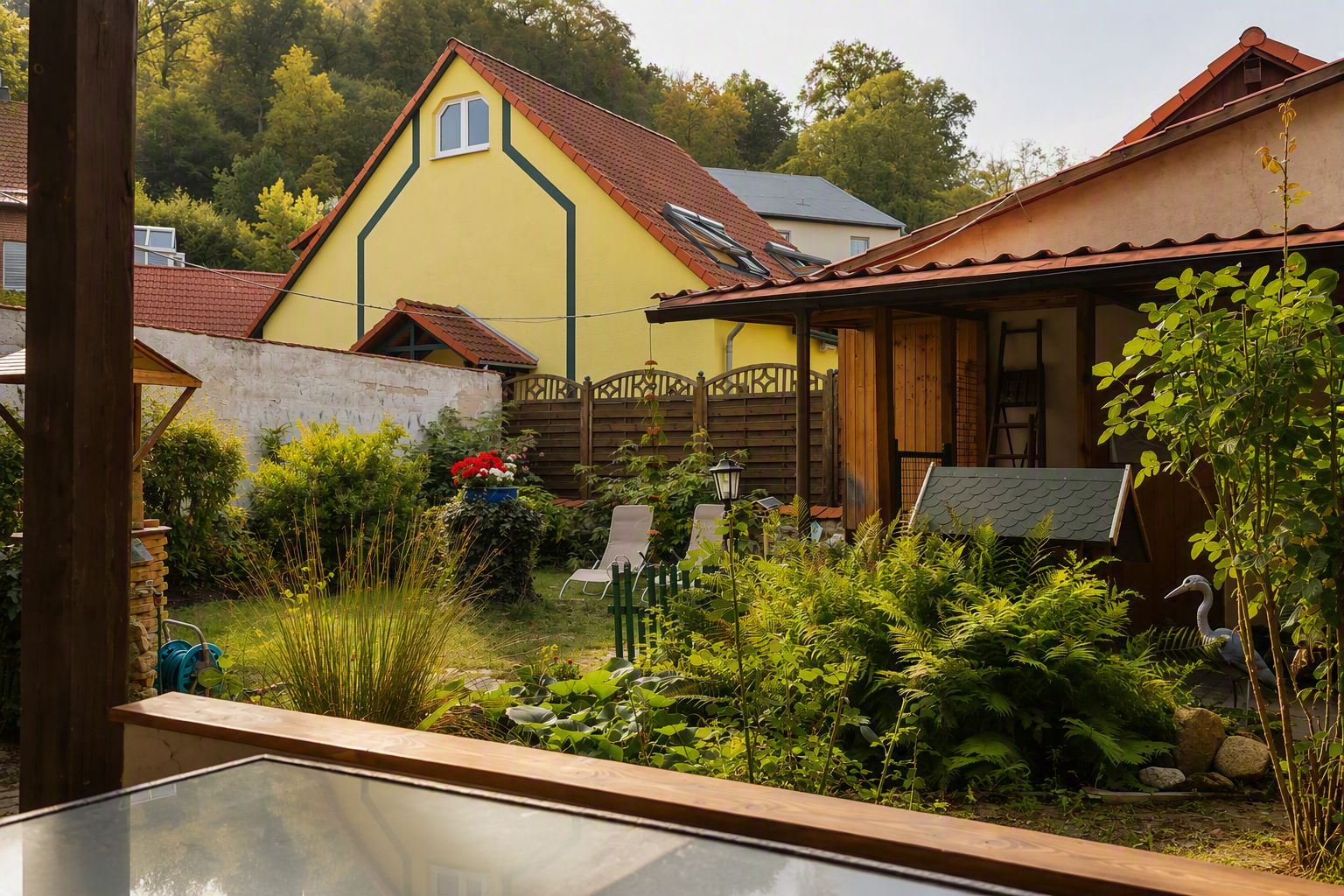 A residential property with a garden, a wooden fence, and a yellow house with a red roof.