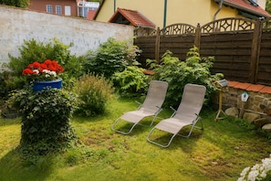 A garden with two metal chairs, a blue planter with red flowers, and a wooden fence. - Garden Retreat – Spacious Apartment by Bodetal (Thale)