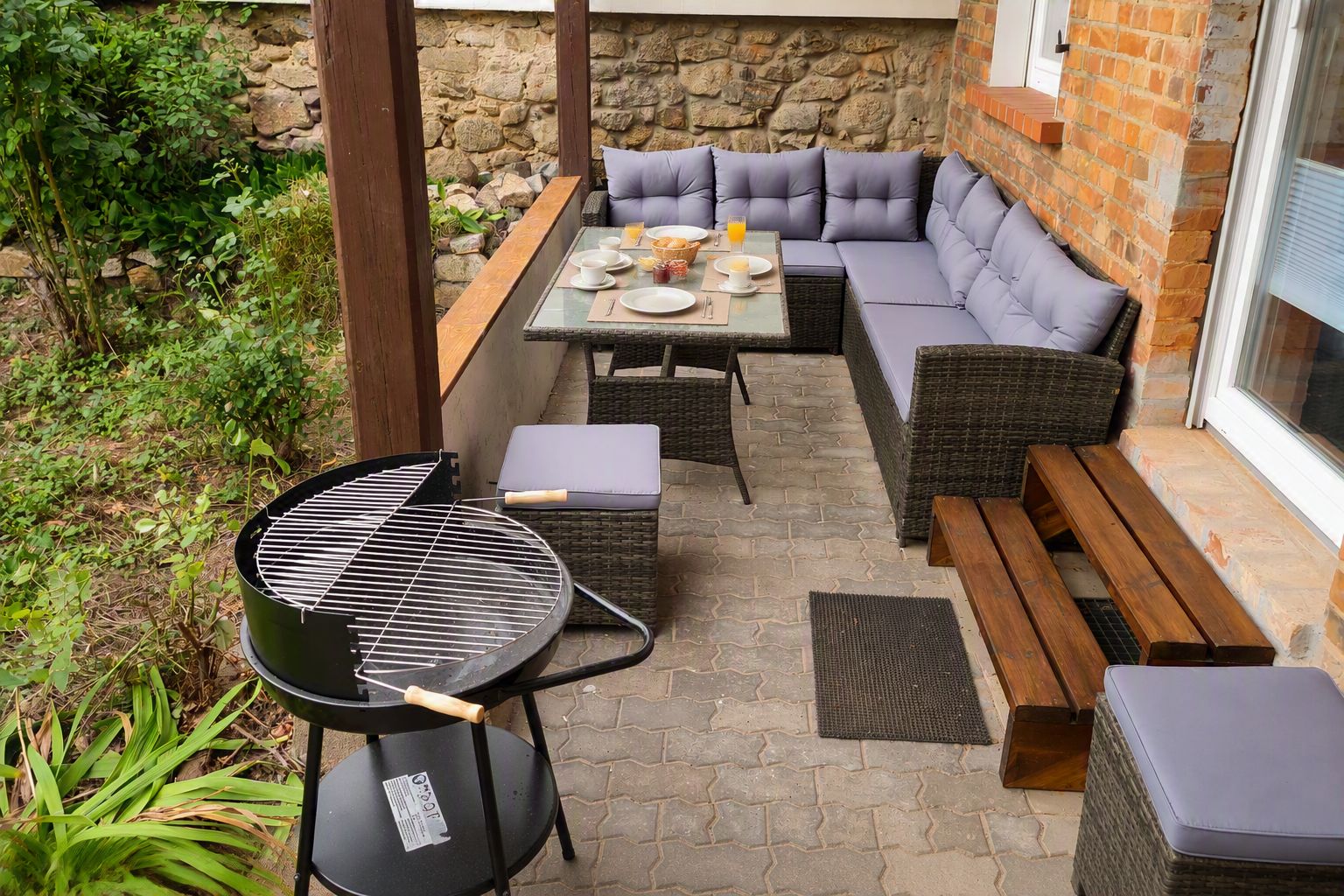 Eine Außenpatio mit Grill, Sitzgelegenheit und einer Wand aus Stein im Hintergrund.