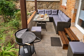En udendørs terrasse med grill, siddepladser og en baggrund af en stenvæg.