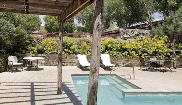 A pool area with lounge chairs, a pergola, and a stone wall with greenery. - Lajitas Golf Resort (Terlingua)