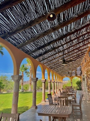 An outdoor patio with wooden tables and chairs, a thatched roof, and a view of the surrounding landscape. - Lajitas Golf Resort (Terlingua)