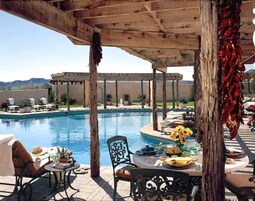 Zona de piscina con área de estar cubierta, una mesa con comida y bebidas, y vistas a la piscina y el paisaje.