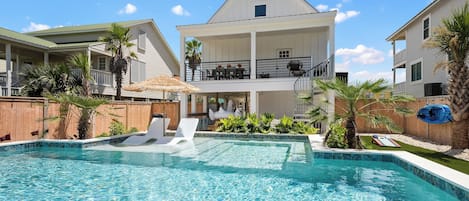 A swimming pool with a hot tub, lounge chairs, and a wooden deck.
