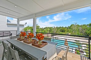 Ein überdachter Essbereich im Freien mit Blick auf einen Pool, ausgestattet mit einem Tisch, Blumenvasen und einem Grill.