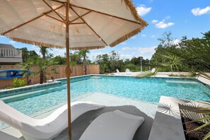 Una piscina con sillas de descanso y un toldo de paja.