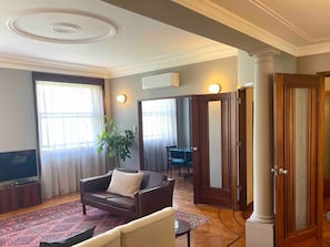 Ein Wohnzimmer mit einer Couch, einem Couchtisch, einem Fernseher und einem großen Fenster mit Vorhängen.