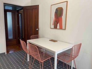 Ein Essbereich mit einem weißen Tisch und vier rosafarbenen Stühlen, einer Holztür und einem gerahmten abstrakten Gemälde an der Wand.