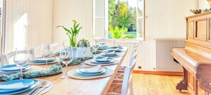 Una mesa de comedor preparada para seis personas, con platos azules y vasos transparentes, rodeada de sillas blancas.