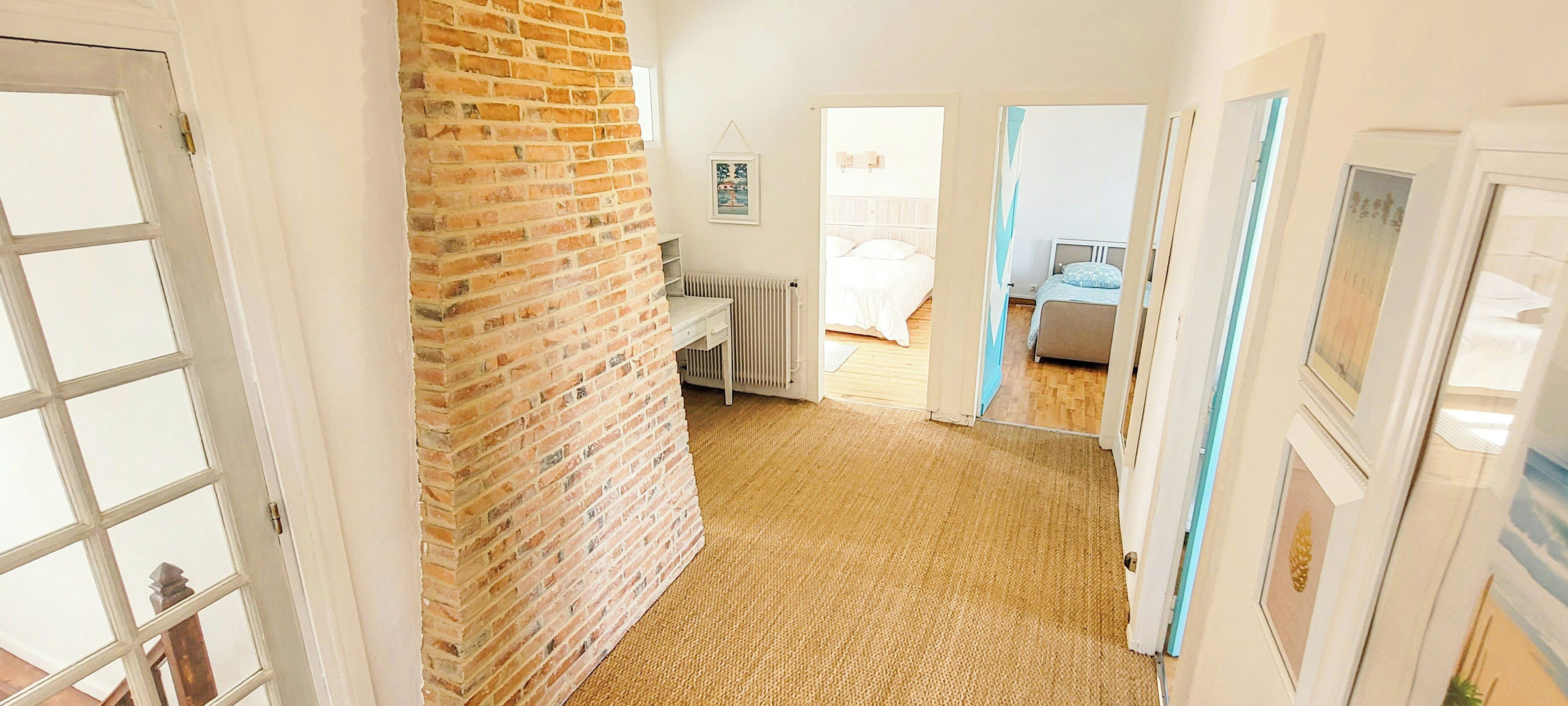 A hallway with a brick wall, a radiator, and a door leading to a bedroom with a bed and a window.