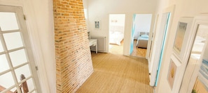 Un pasillo con pared de ladrillo, un radiador y una puerta que da a un dormitorio con cama y ventana.