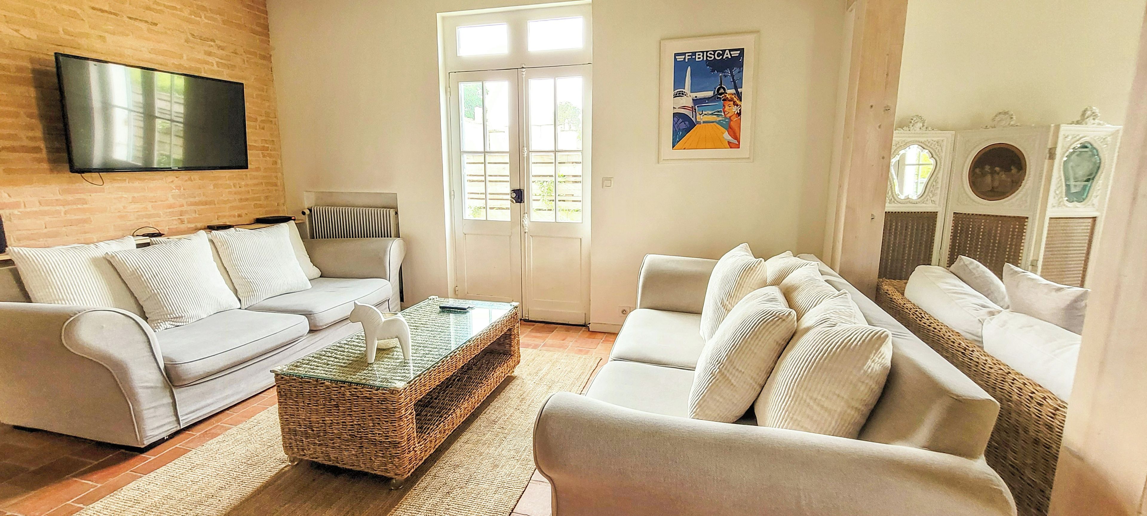 Un salon comprenant un canapé, des fauteuils, une table basse et un téléviseur fixé à un mur en briques.