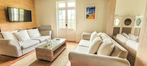 A living room with a sofa, armchairs, a coffee table, and a television mounted on a brick wall. - Former bakery between forests and ocean at Lüe (LÜE)