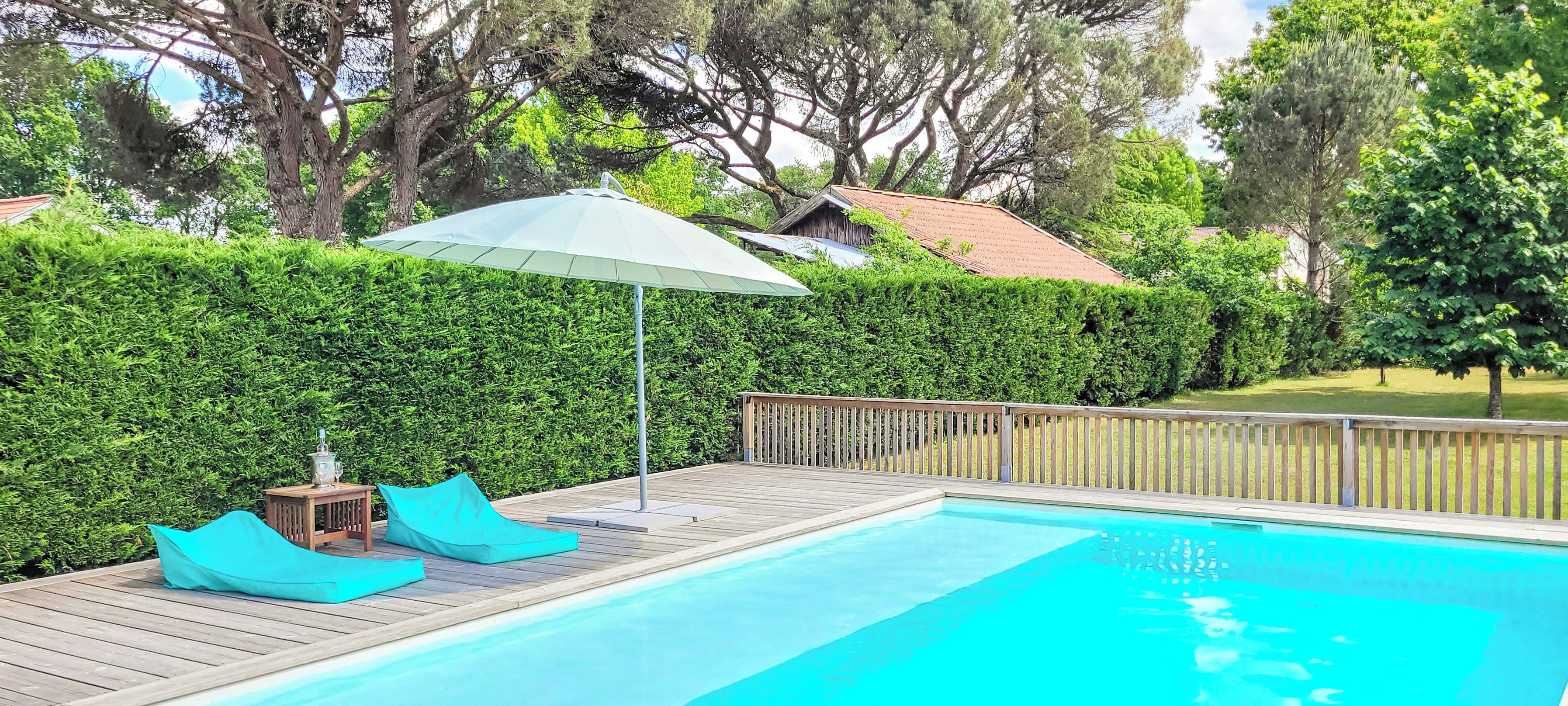 Une piscine avec une terrasse en bois, une table et des chaises, et un grand parasol.
