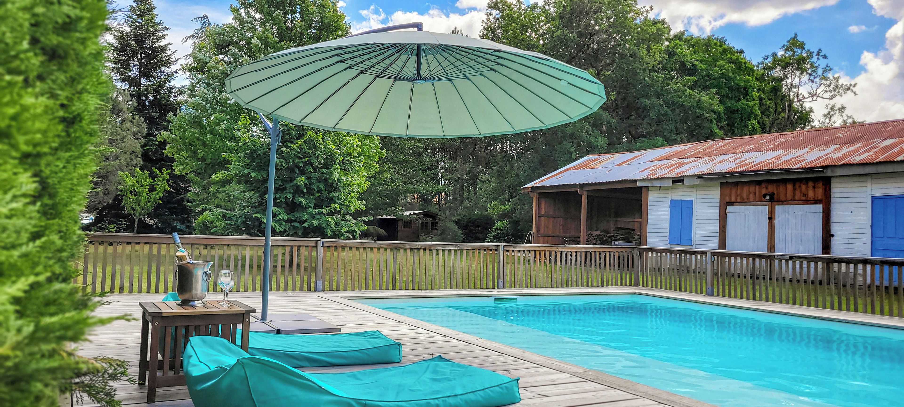 Une piscine avec une terrasse en bois, des chaises longues et un parasol.