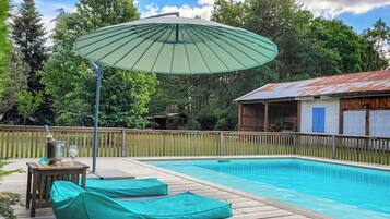 Une piscine avec une terrasse en bois, des chaises longues et un parasol.