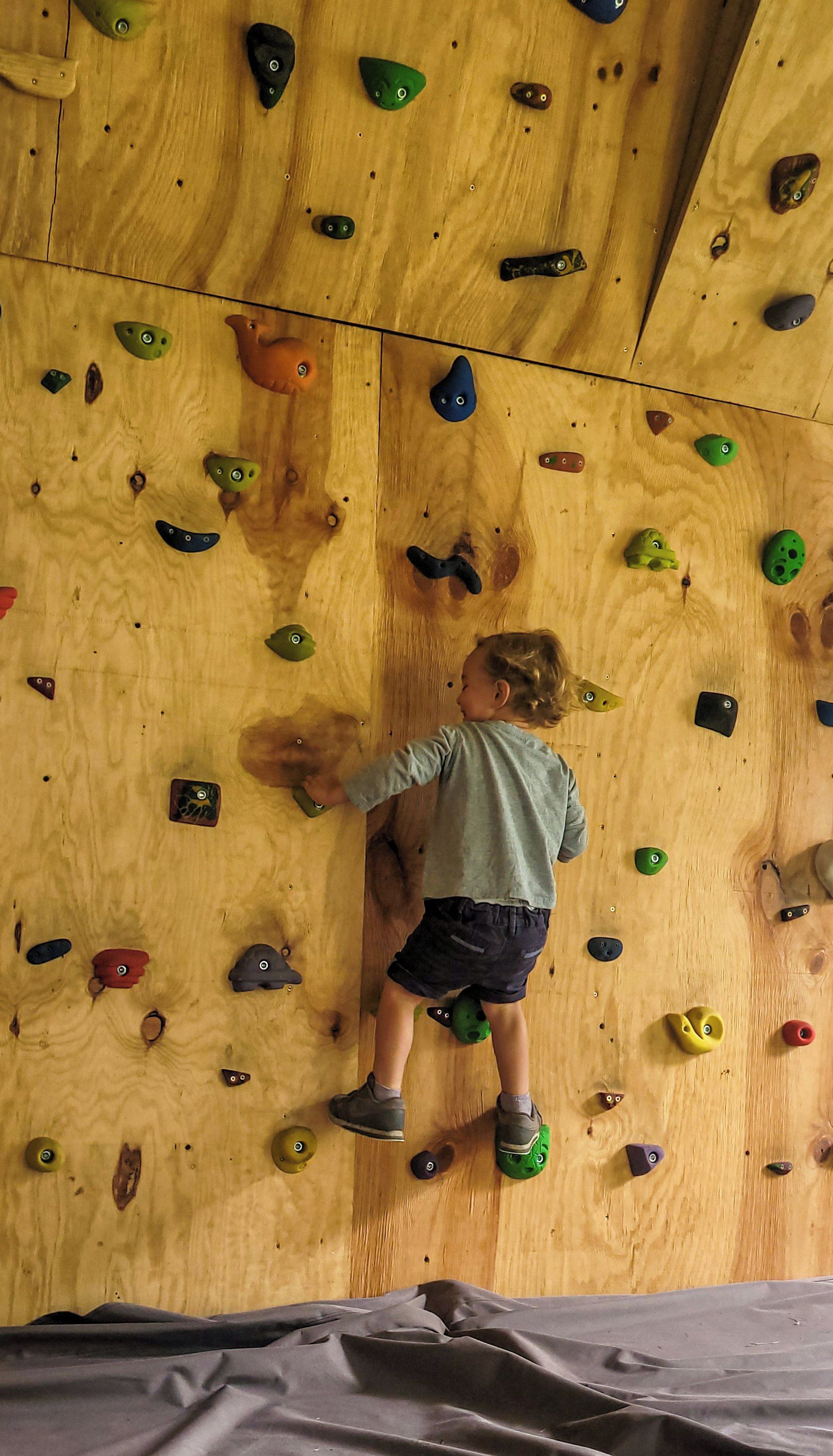 A child climbing a wooden wall with variously shaped holds.