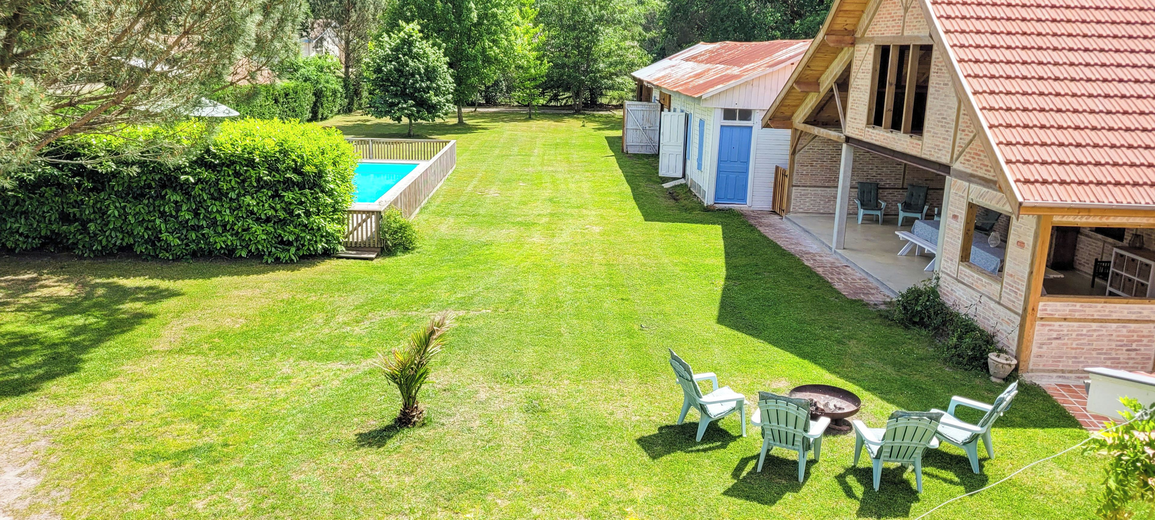 Une pelouse bien entretenue, agrémentée d’une piscine, d’un espace salon extérieur et d’un bâtiment rustique doté d’un toit rouge.