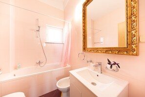 Een badkamer met een bad, toilet, wastafel en een grote spiegel met een versierde lijst.
