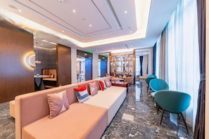 A modern hotel lobby with a long sofa, a small dining area, and a bookshelf.