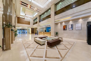 A spacious lobby with a reception desk, seating area, and a high ceiling with decorative lighting.