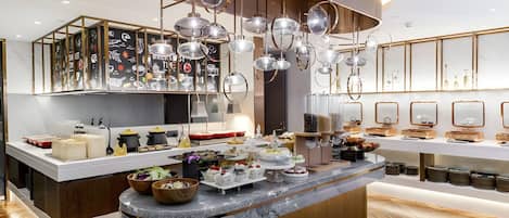 A modern kitchen with a central island, overhead lighting, and a variety of food items displayed.