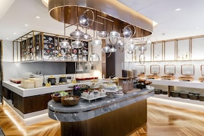 A modern kitchen with a central island, overhead lighting, and a variety of food items displayed.