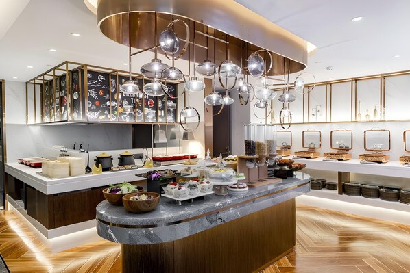 A modern kitchen with a central island, overhead lighting, and a variety of food items displayed.
