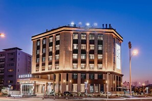 A multi-story hotel with a corner entrance, illuminated signage, and a visible entrance canopy.