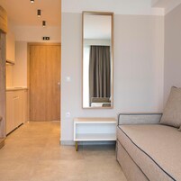 A hotel room with a wooden door, a white console table, a beige sofa, and a large mirror on the wall.