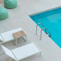 Un área junto a la piscina con piscina, dos sillas reclinables blancas, una mesa pequeña y dos sillones de tina verdes.