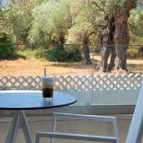 Un vaso de café helado sobre una mesa redonda, con vistas a árboles y una valla de celosía blanca.