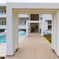 A modern outdoor pool area with a clear pathway leading to a building entrance, surrounded by white walls and a covered seating area.