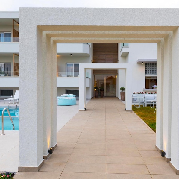 A modern outdoor pool area with a clear pathway leading to a building entrance, surrounded by white walls and a covered seating area. - Motivo Thassos (Thasos)